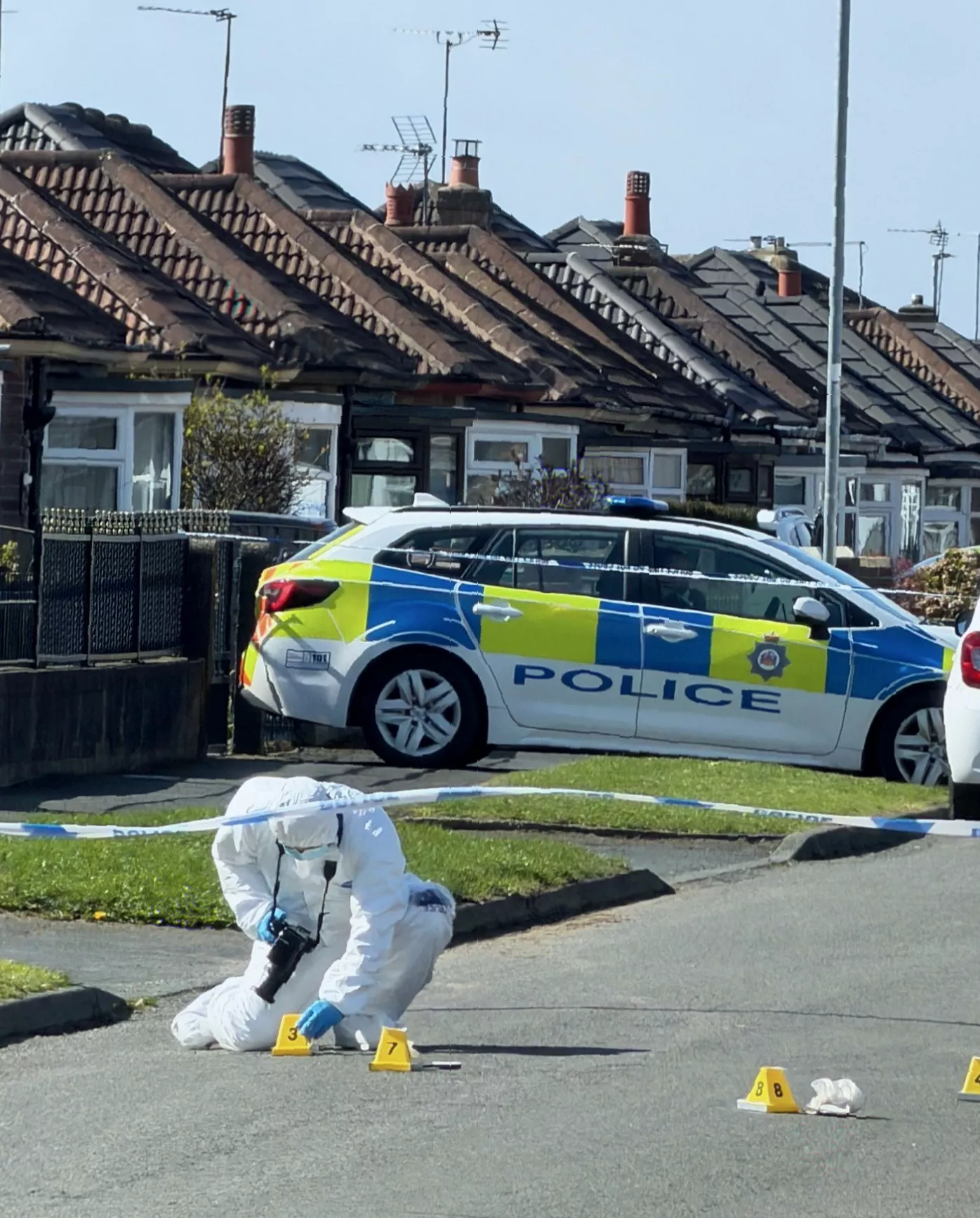 A forensic officer at work on a pavement in a suburban neighbourhood.