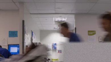 A doctor in NHS scrubs reviewing medical notes in a hospital corridor.