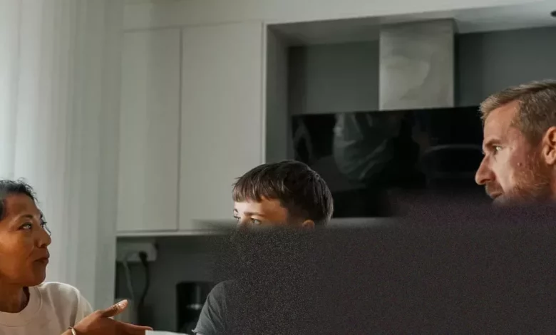 Parents and a young adult discussing finances over a kitchen table.