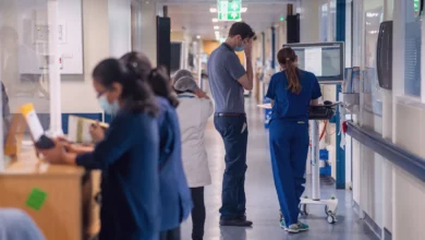 A busy NHS hospital corridor with medical staff and patients.