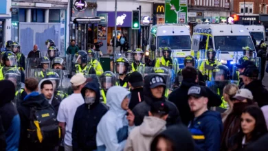 Riot police with shields facing a crowd on an Epsom street at night.