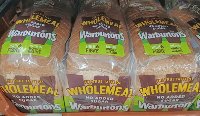 Close-up of a UK supermarket shelf with various bread packaging labels.