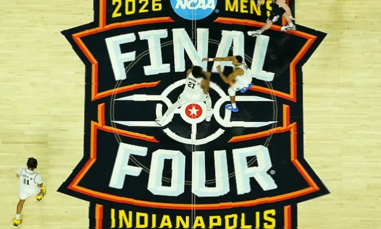 Basketball arena with fans seated as March Madness tournament games are displayed on a large screen above the court.