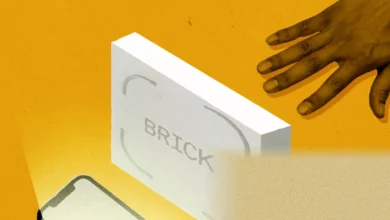 A small plastic puck device called Brick sits on a wooden table next to a smartphone