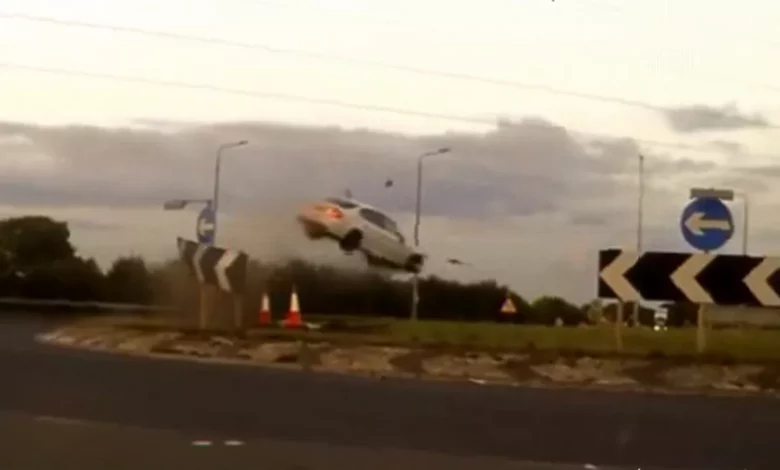 Police dashcam footage of a car crash on a roundabout at night.