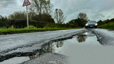 A large SUV driving on a British road riddled with potholes.