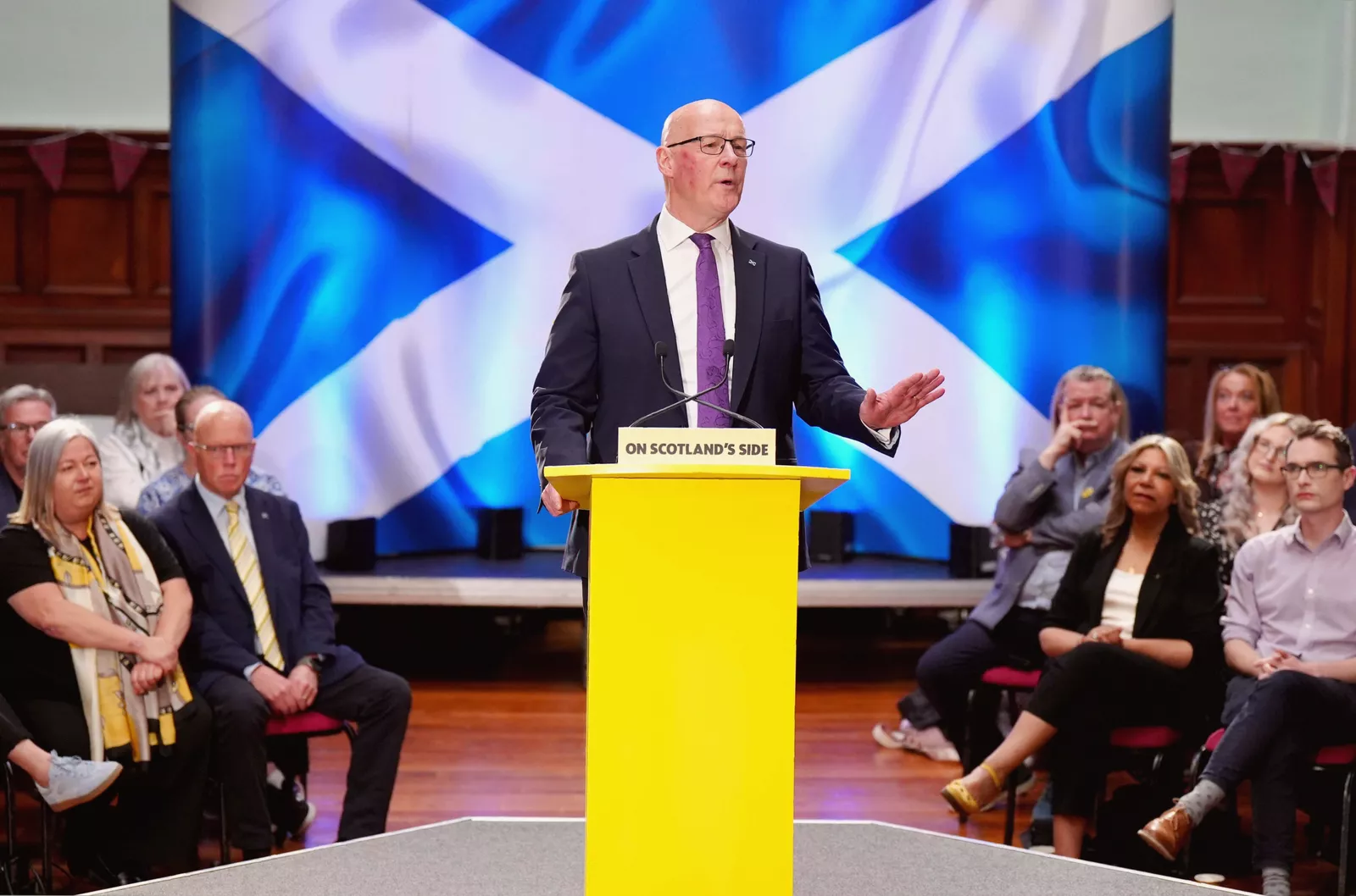 A crowded Holyrood election campaign event with party leaflets and banners on display.