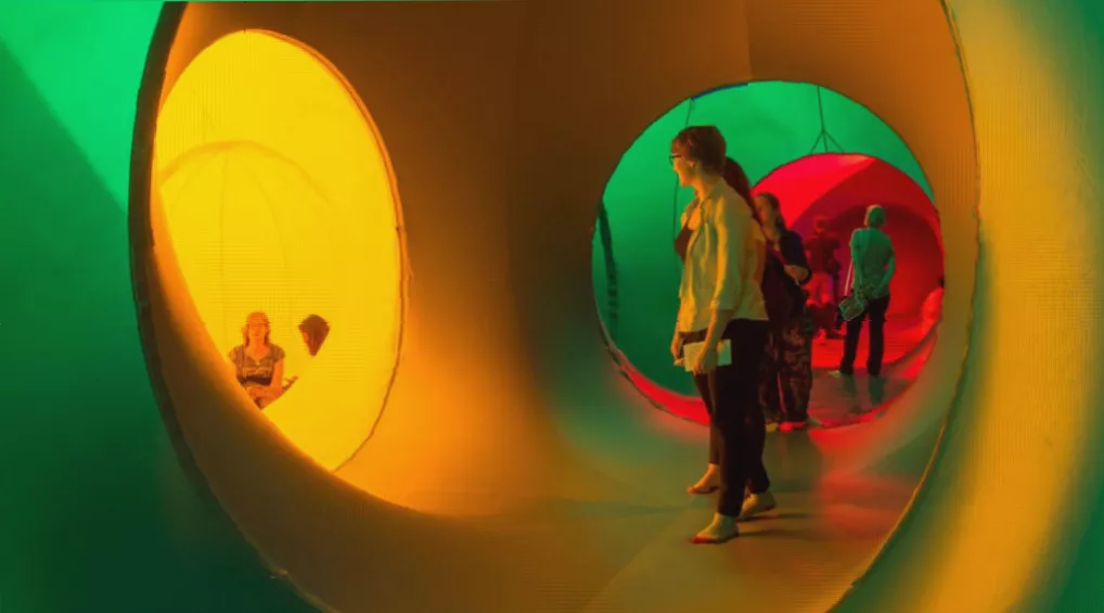 Visitors walking through colourful illuminated chambers inside the Luminarium