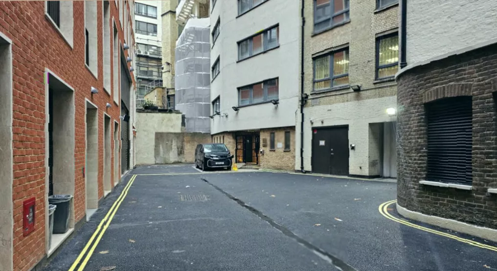 Scuffed metal cladding on a building corner in a mews, showing marks from historic delivery vehicles.