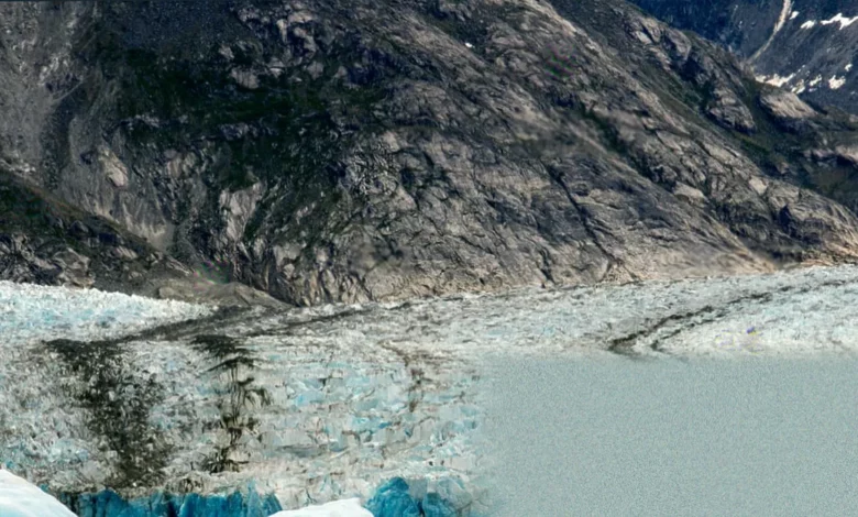 A narrow Alaskan fjord surrounded by steep, ice-covered mountains and receding glaciers.