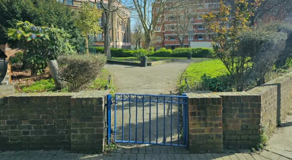 Blue LDDC-era gates at the entrance to the pocket park, slightly faded from years of exposure
