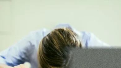 A school headteacher sitting alone at a cluttered desk, exhaustion visible in their posture