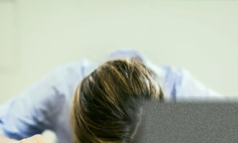 A school headteacher sitting alone at a cluttered desk, exhaustion visible in their posture