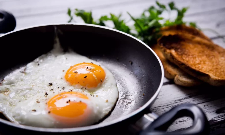 A person cracking an egg into a frying pan in a home kitchen