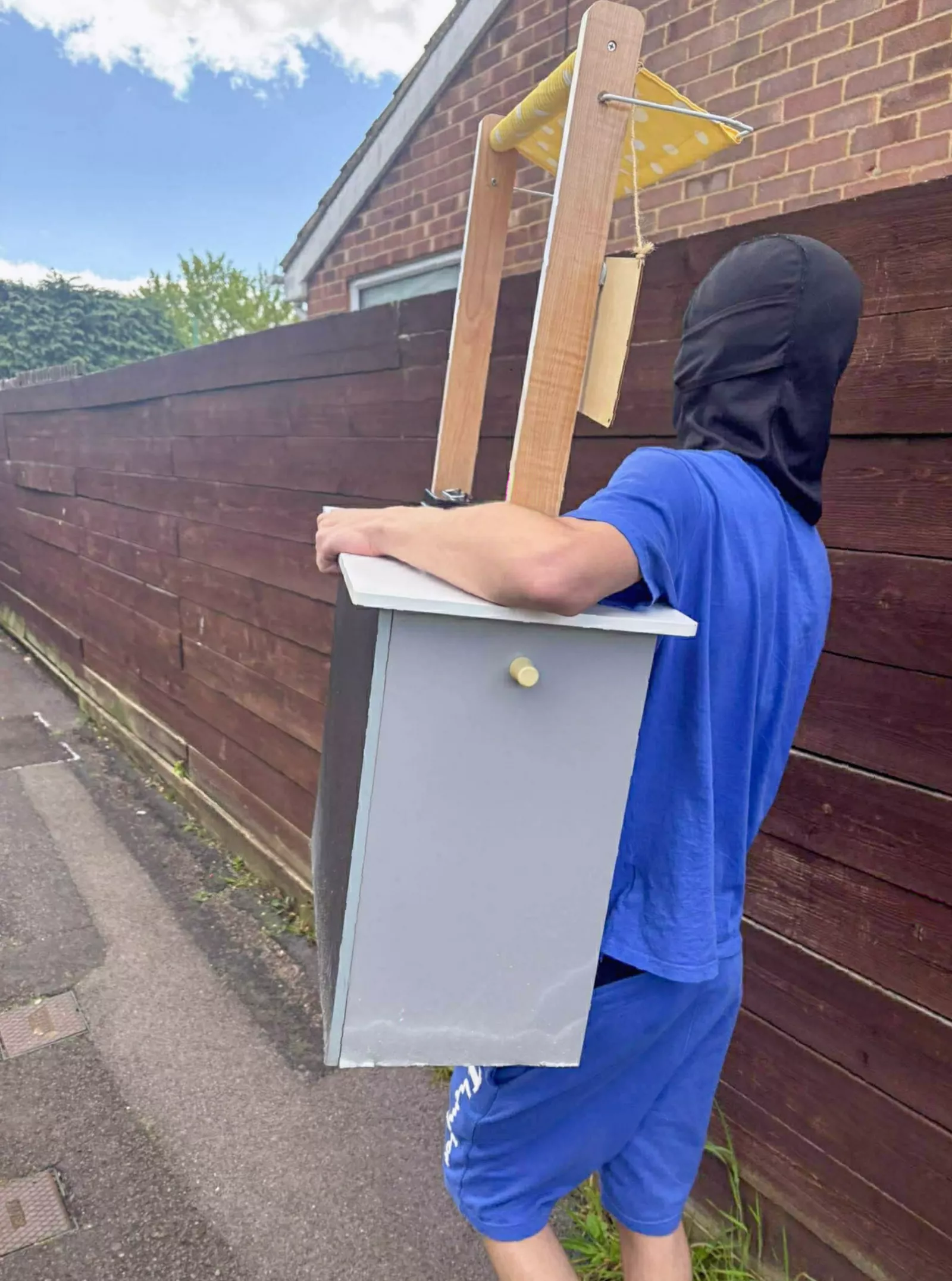 Two teenagers in balaclavas running away from a house carrying a small wooden shop front