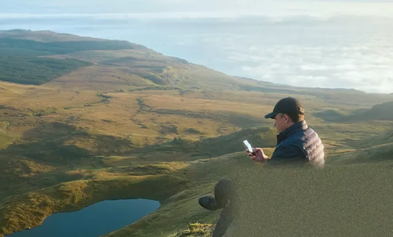 Person holding a smartphone with no signal bars while standing on a rural footpath