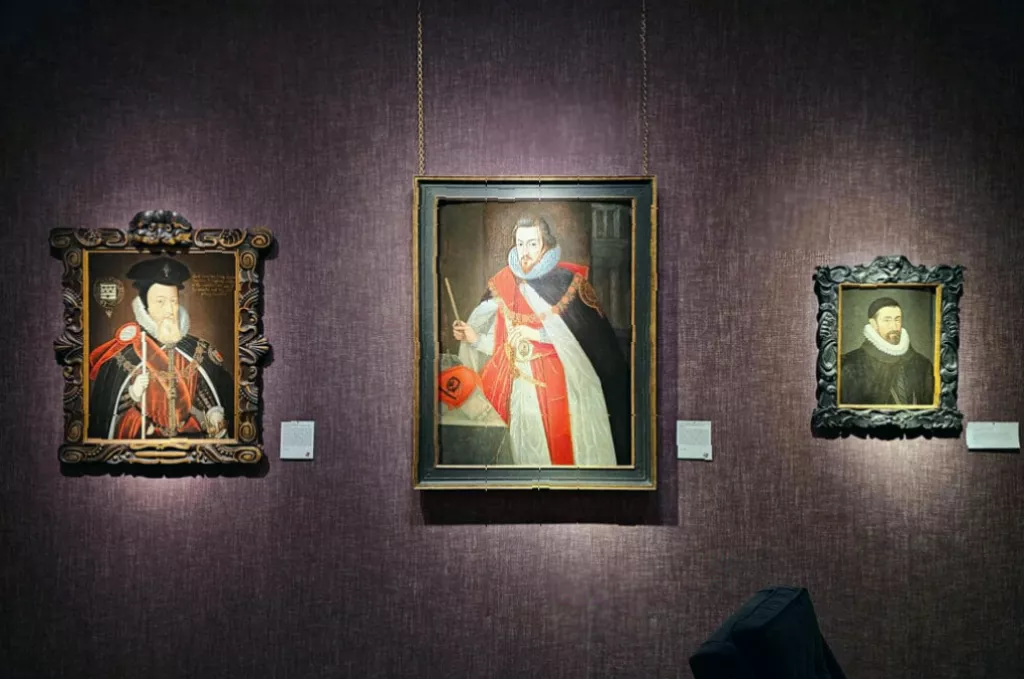 Elizabeth I portrait surrounded by courtiers' paintings in a gallery room