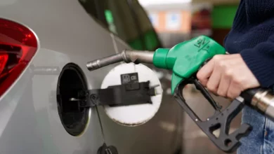 A petrol station forecourt with cars queuing at fuel pumps on a rainy day