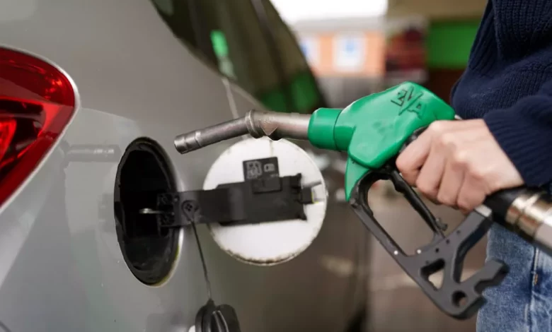 A petrol station forecourt with cars queuing at fuel pumps on a rainy day