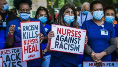 A black female nurse in a hospital uniform speaking on a telephone at a nursing station