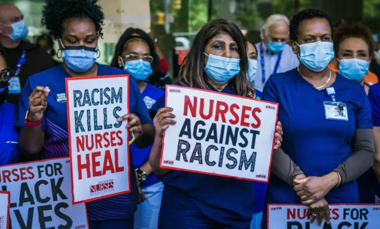 A black female nurse in a hospital uniform speaking on a telephone at a nursing station