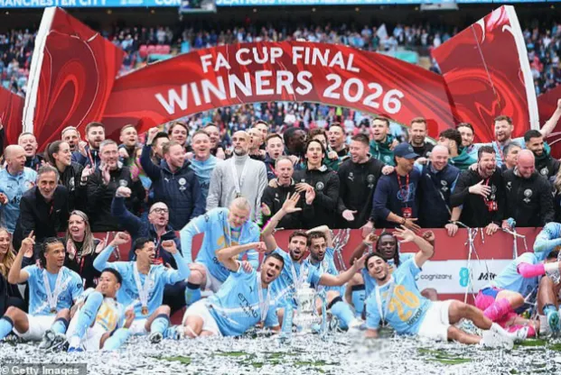 Manchester City players lifting the FA Cup trophy on the pitch at Wembley