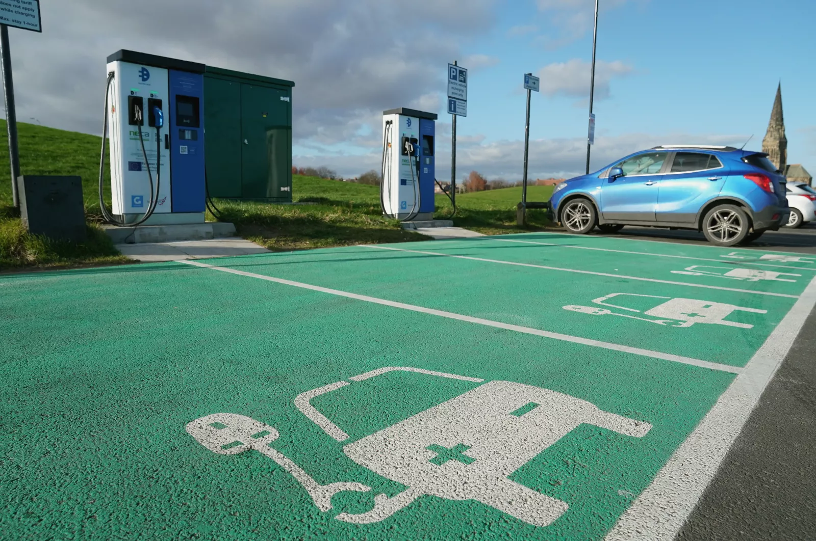 An electric car parked beside a public chargepoint in a remote village with no nearby buildings