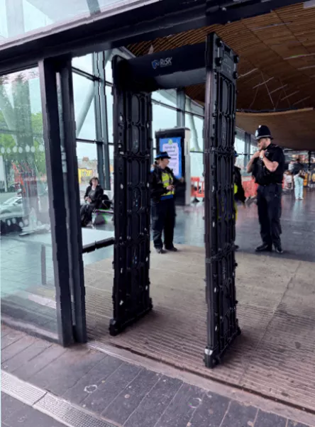 A mobile phone and keys tray beside a knife arch at a secondary school safeguarding checkpoint.
