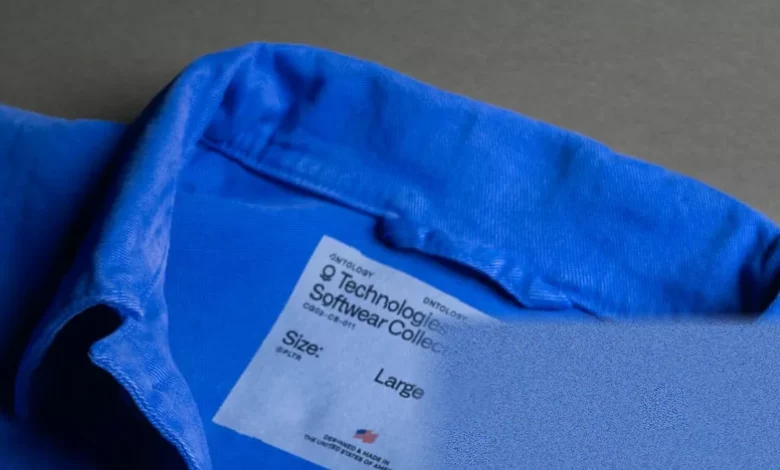 A denim chore coat with a tech company logo on the chest pocket displayed on a mannequin