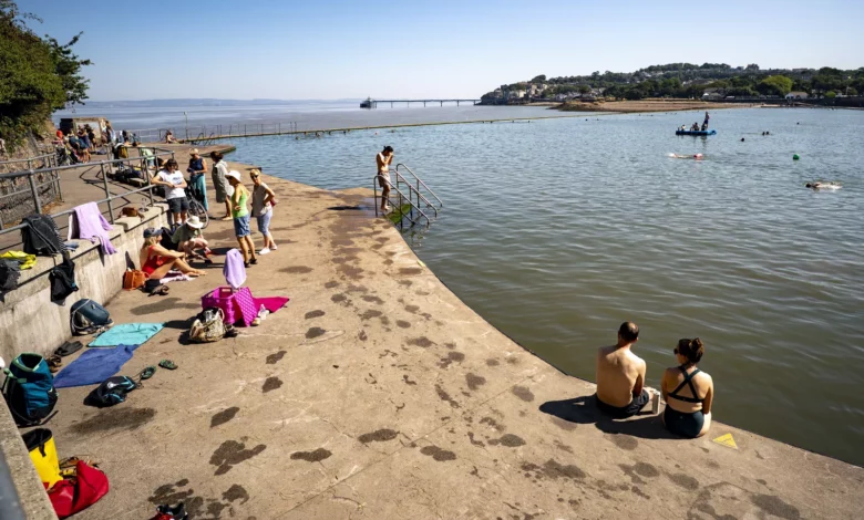 A beach on a sunny bank holiday with families applying sunscreen and seeking shade under umbrellas