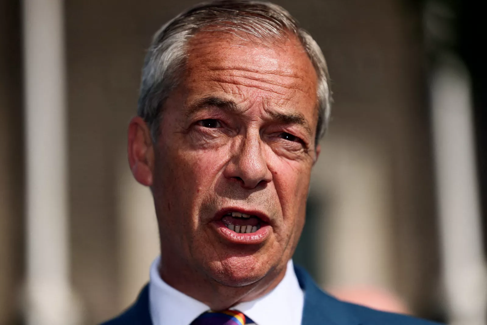 A politician gestures while speaking at a lectern during a campaign event in a town hall setting.