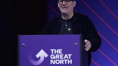 A press conference in Leeds where a politician speaks at a podium with European Union flags behind him.
