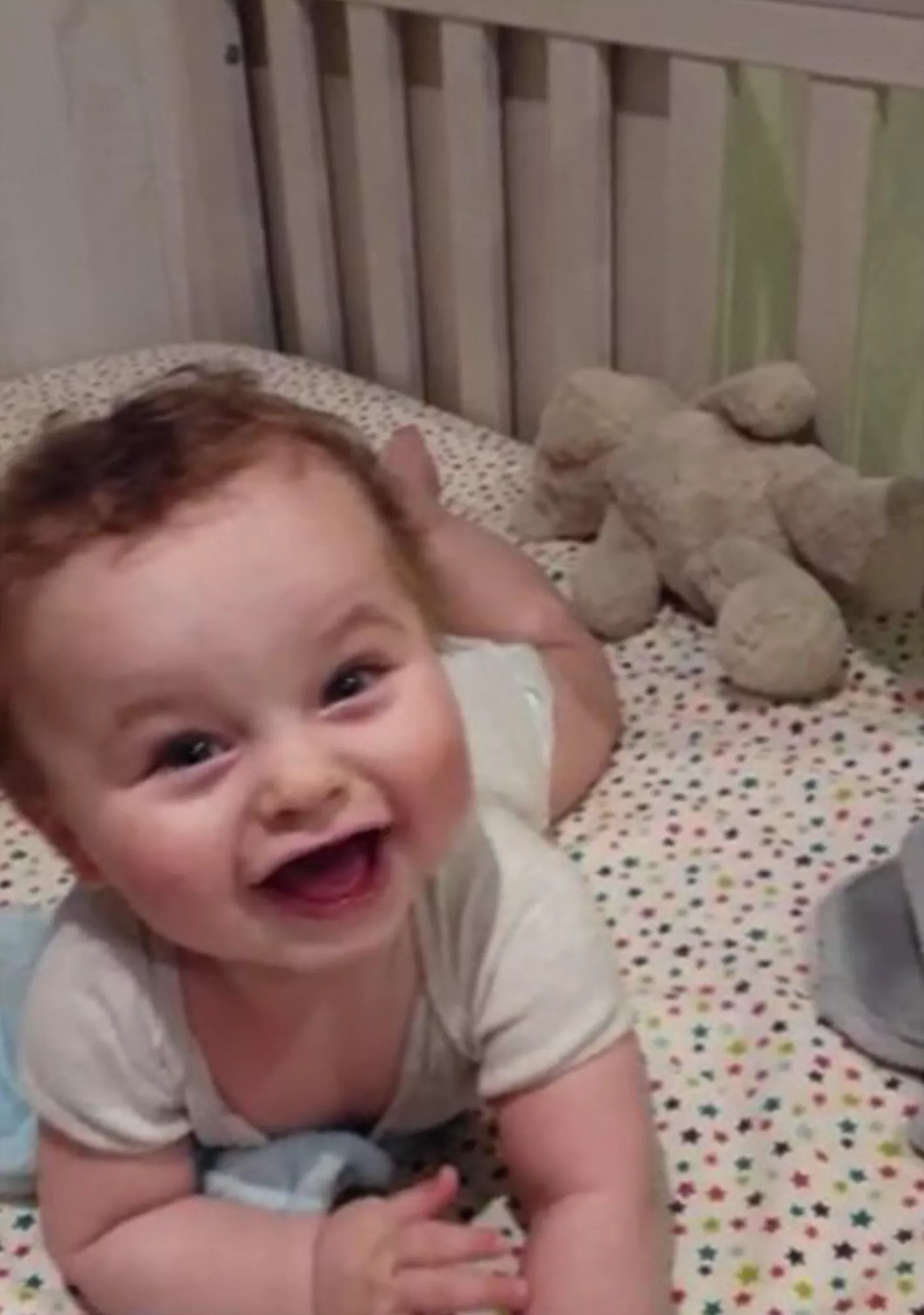Baby cot with head and arms over the top bar in an unsafe position