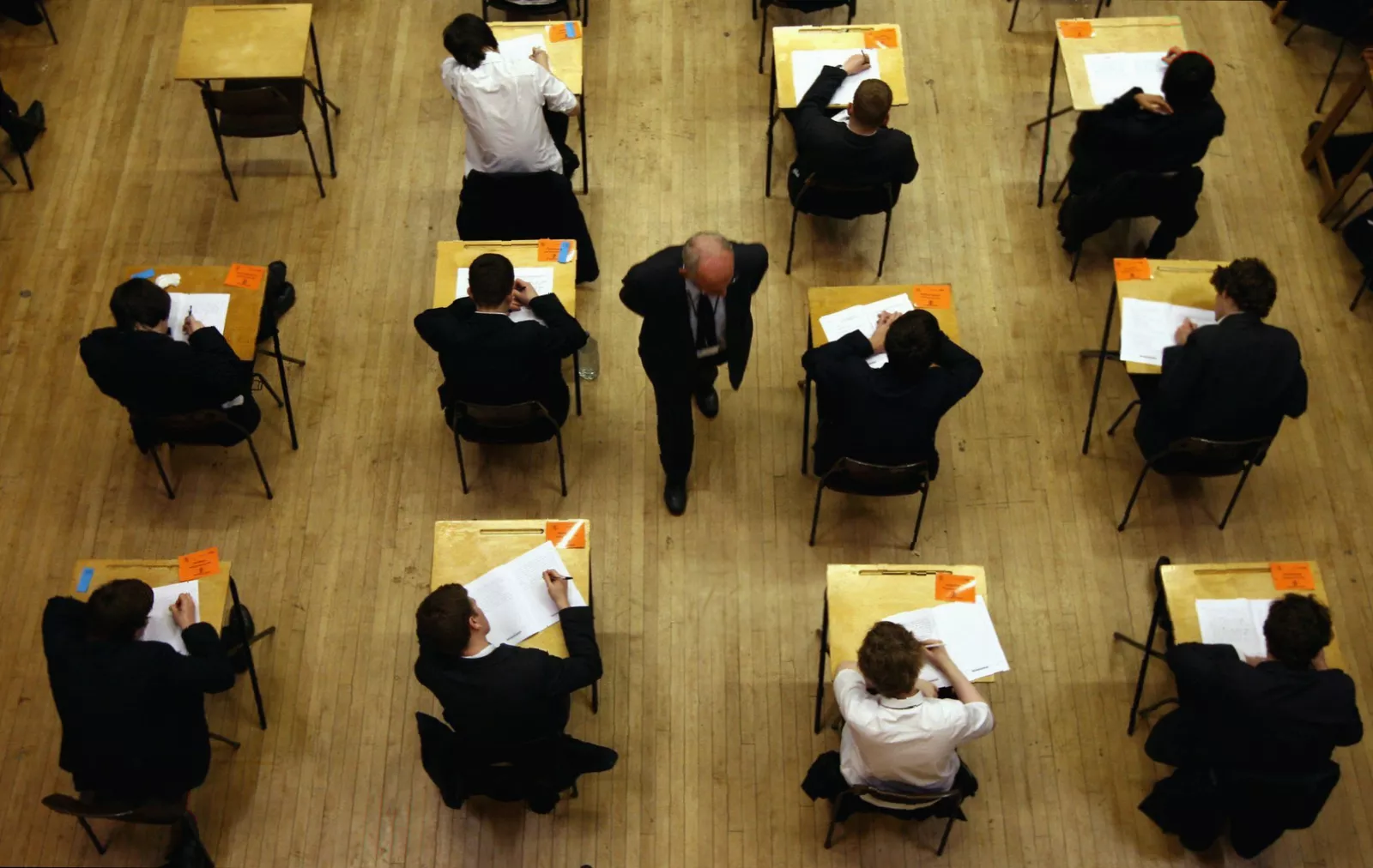 A pile of completed exam papers and stationery on a classroom desk