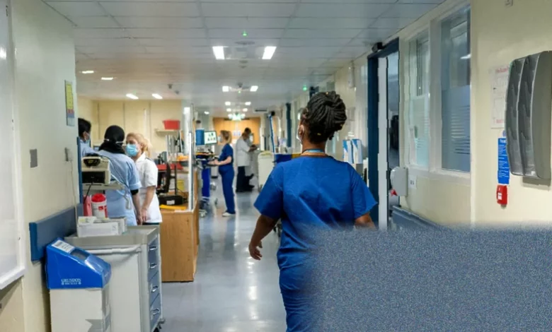 Hospital ward corridor with nurses walking quickly past empty patient bays