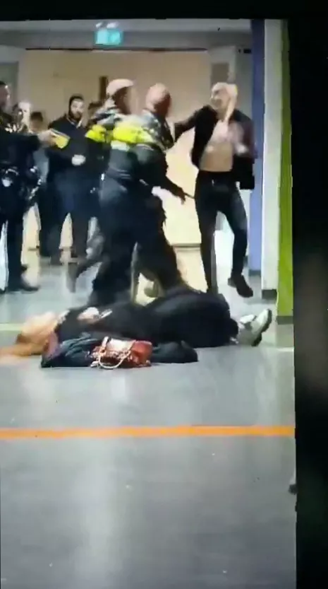 Dutch police officers restraining a man on the ground as a confrontation unfolds in a hallway