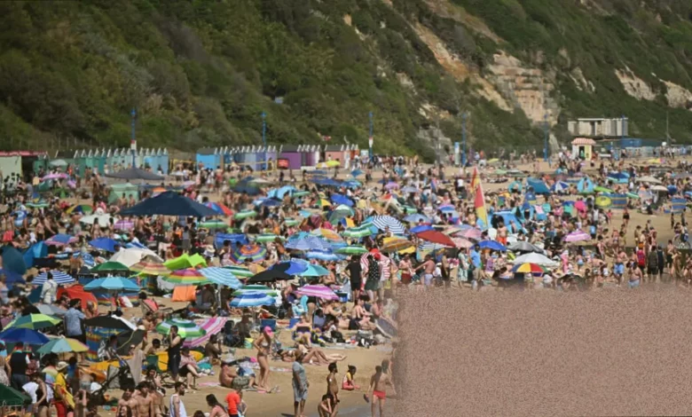 Crowded lakeside beach during a UK heatwave with people swimming in open water