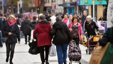 Shoppers walking past a row of shops with sale signs in a Welsh high street.