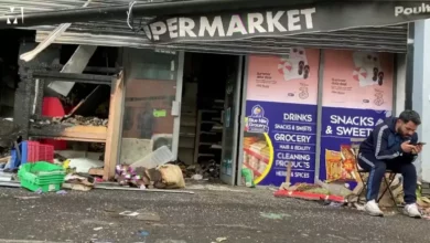 Burnt-out entrance of a Belfast supermarket with shattered metal gates after a night of rioting