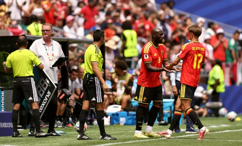 A World Cup pitch with stadium floodlights and team flags ahead of Belgium versus Iran.