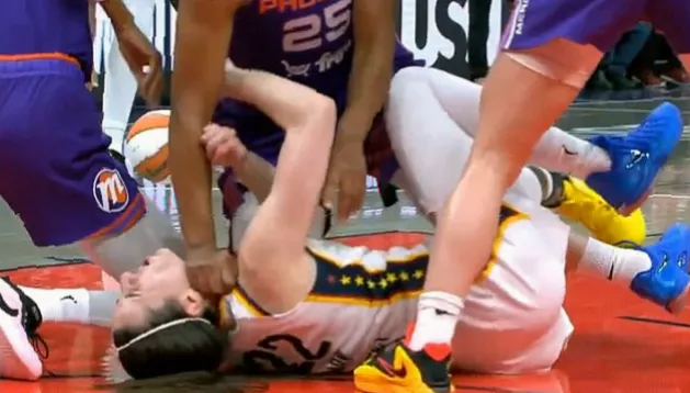 Crowd in an indoor arena watching intently as a player lies on the court following a collision.