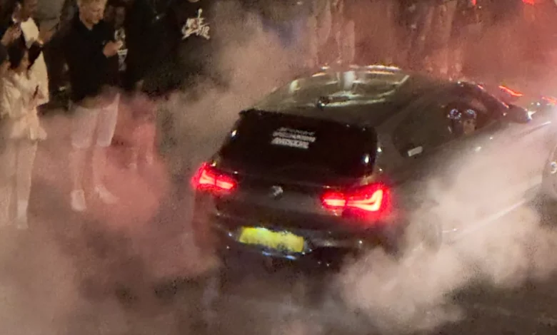 Night-time car meet on a central London street with spectators filming on phones