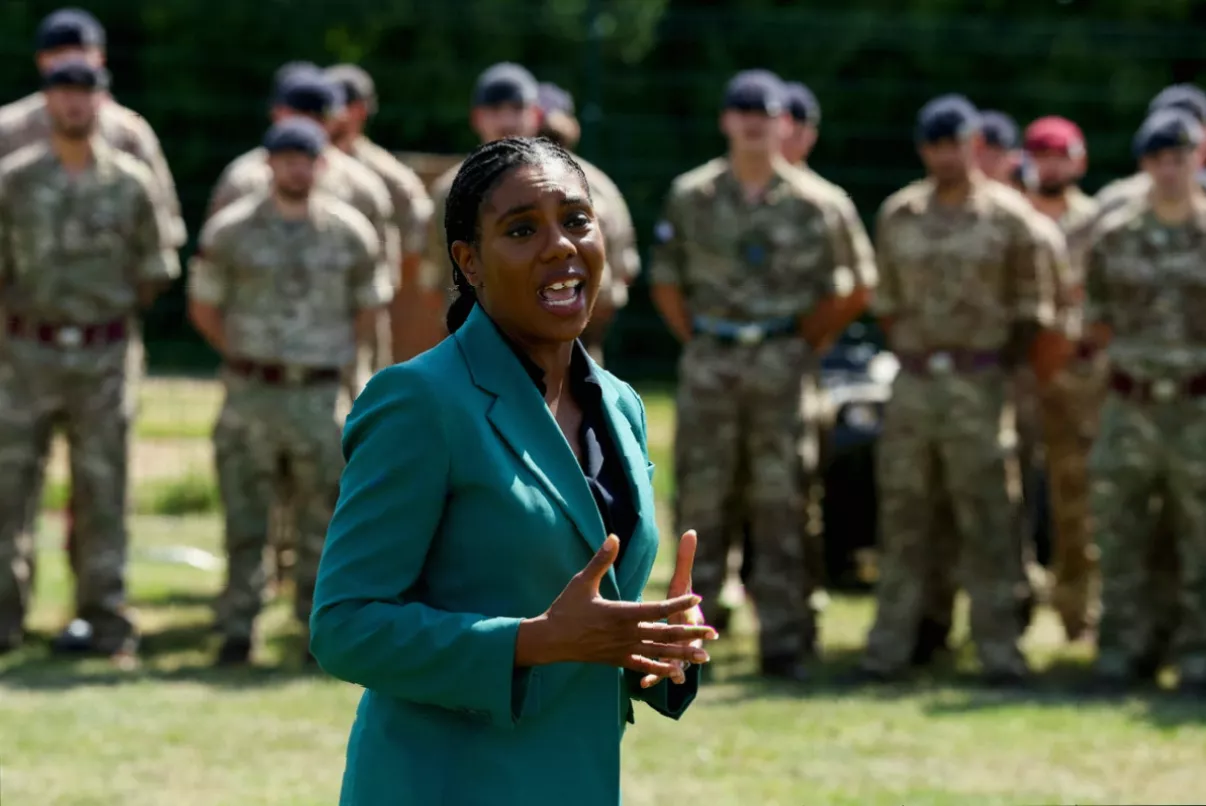 A politician speaking at a podium with Union Jack flags and defence policy documents visible