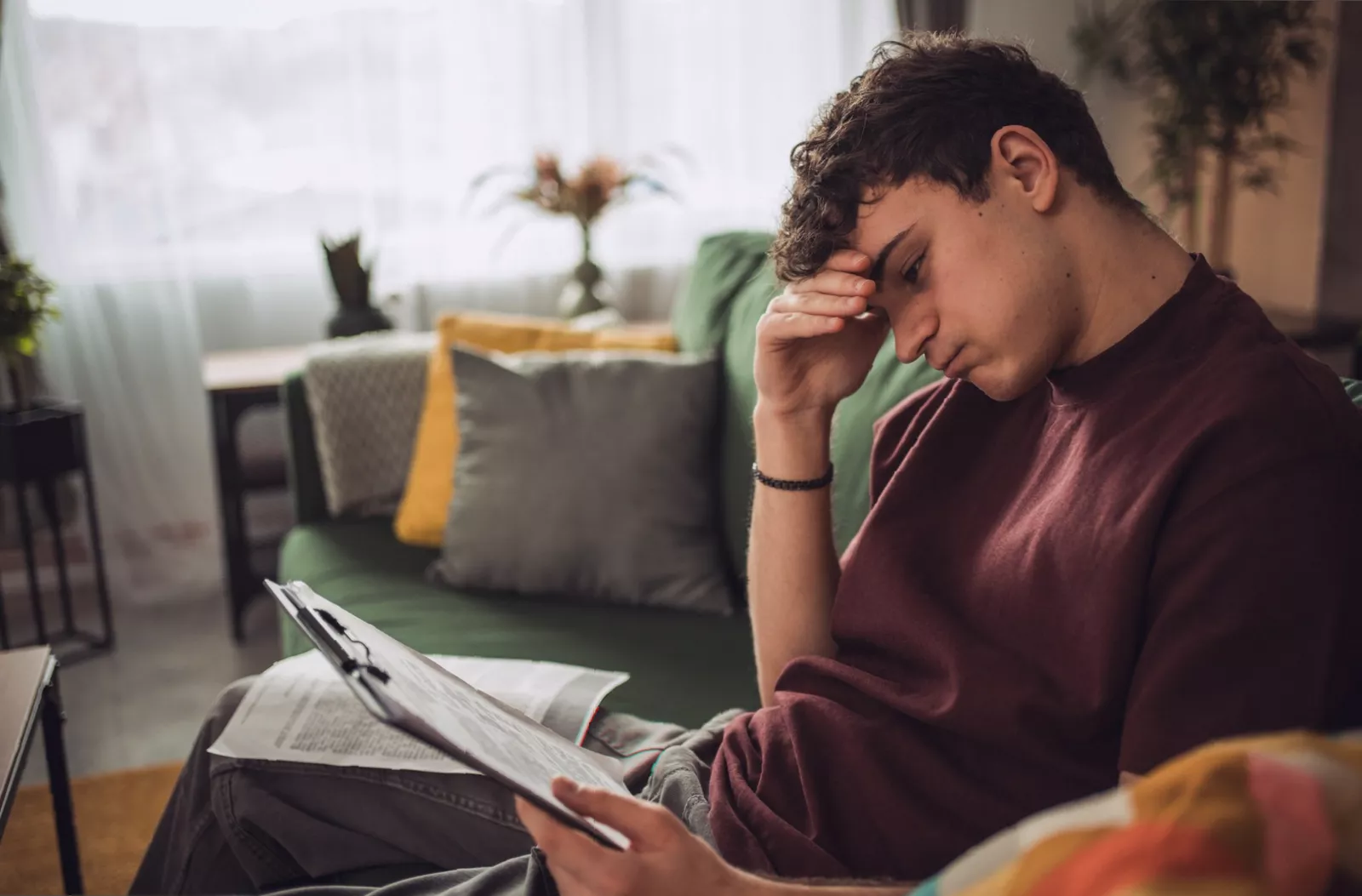 A young adult in a rented flat in Britain, looking at bills on a kitchen table while using a calculator.