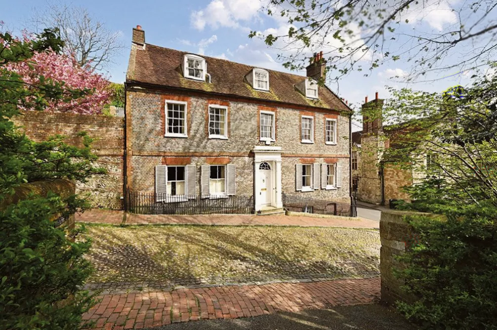 Octagonal summer house with a tiled roof set within a walled garden behind a historic property.