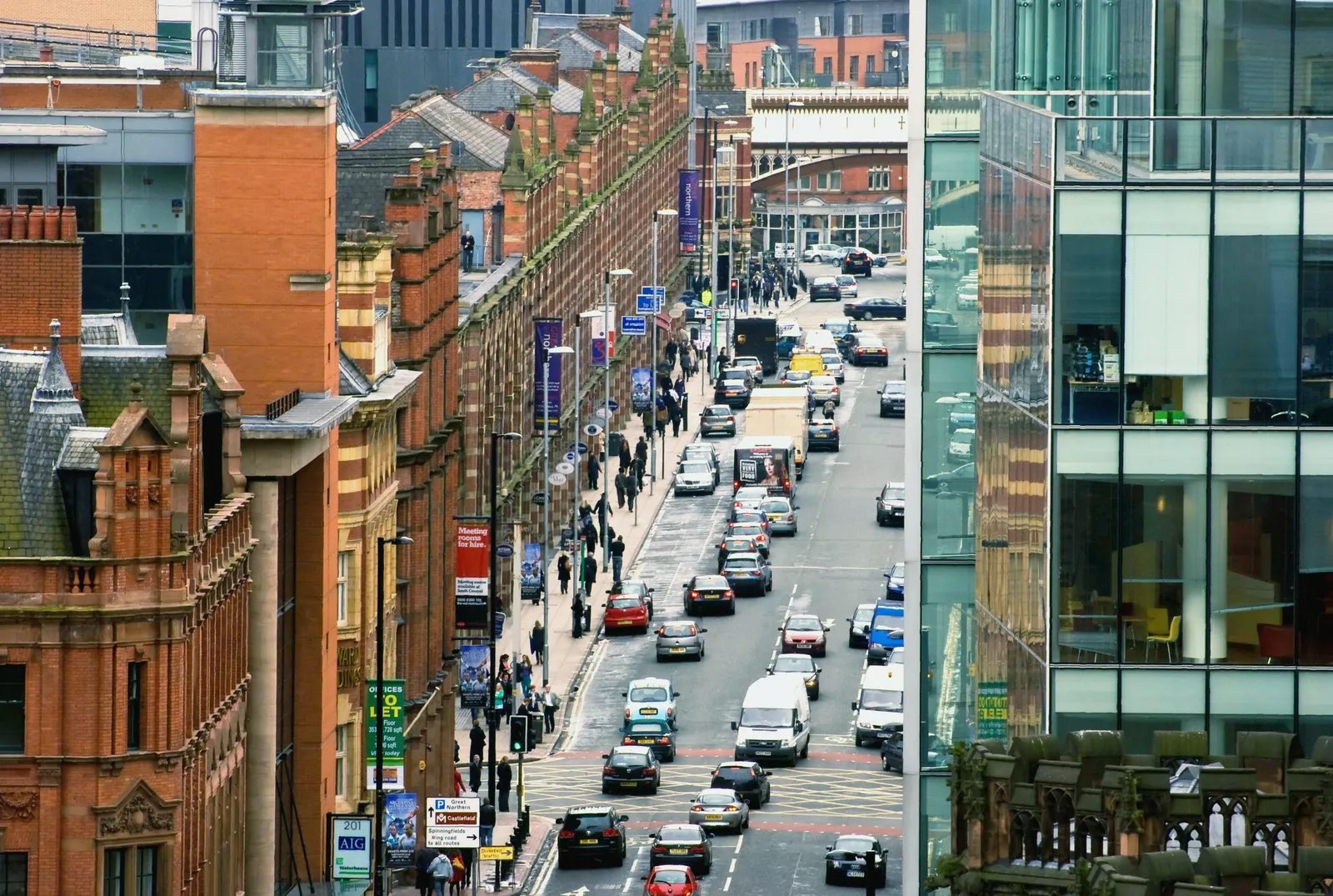 A residential street with parked cars and newly planted trees along wider pavements