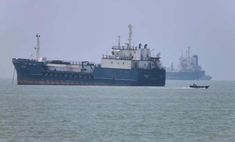 A warship navigates through the narrow Strait of Hormuz under a hazy sky.