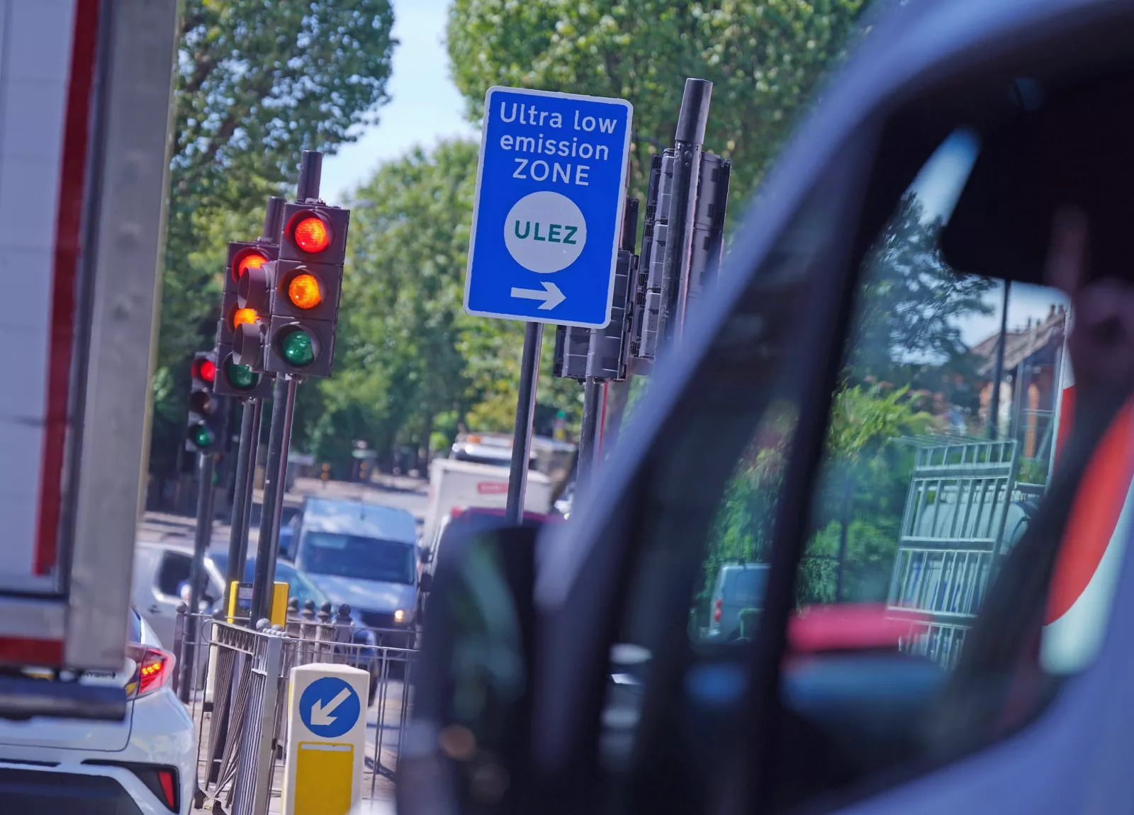 A Ulez sign and camera on a London street with traffic passing underneath