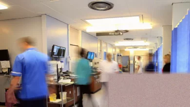 Crowded hospital emergency department waiting area with patients on chairs and staff at a counter in England.