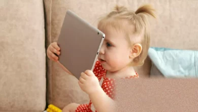 A baby lying on a play mat next to a smartphone on the floor.